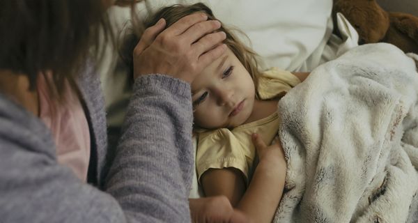 Mutter, hält eine Hand auf die Stirn ihrer kranken Tochter.