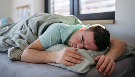 Mann, liegt im Bett und schläft.