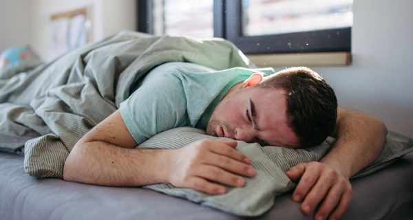 Mann, liegt im Bett und schläft.