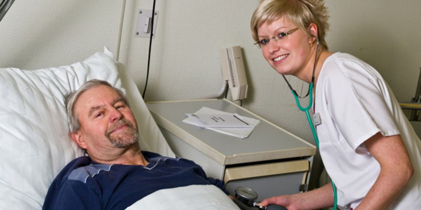 Mann im Krankenbett bekommt von Schwester den Blutdruck gemessen.