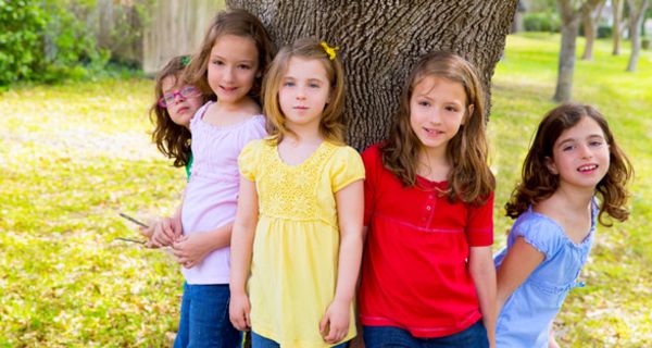 Fünf Mädchen ca. 8, 9 Jahre alt, stehen mit dem Rücken im Kreis um einen Baum herum