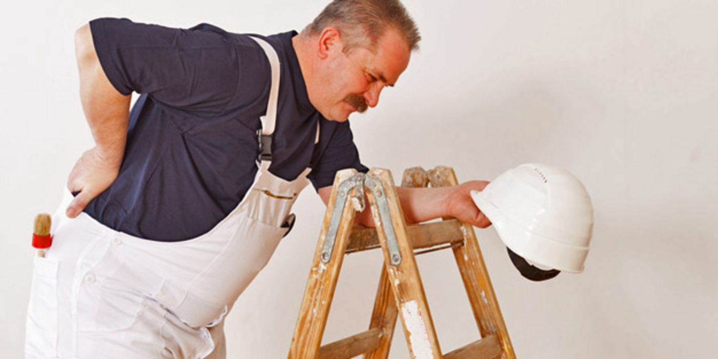 Bauarbeiter stützt sich an einer Leiter ab und hält sich den schmerzenden Rücken