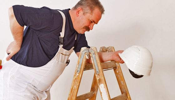 Bauarbeiter stützt sich an einer Leiter ab und hält sich den schmerzenden Rücken