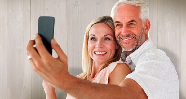 Attraktives, jugendlich wirkendes Seniorenpaar (Frau ca. 60+ Mann ca. Ende 60, weiße Sommerkleidung, leicht gebräunt) machen ein Selfie