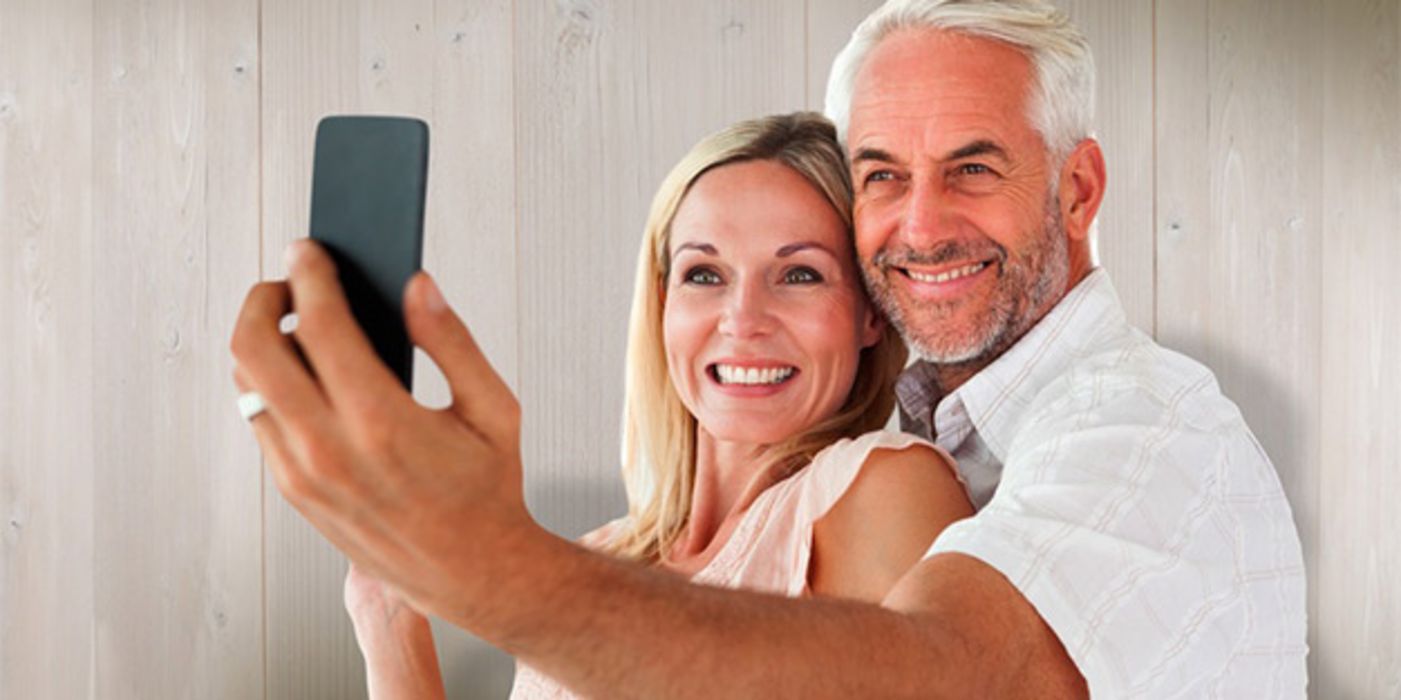 Attraktives, jugendlich wirkendes Seniorenpaar (Frau ca. 60+ Mann ca. Ende 60, weiße Sommerkleidung, leicht gebräunt) machen ein Selfie