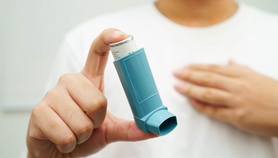 Frau, hält ein Asthmaspray in die Kamera.