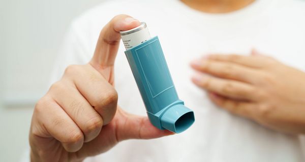 Frau, hält ein Asthmaspray in die Kamera.