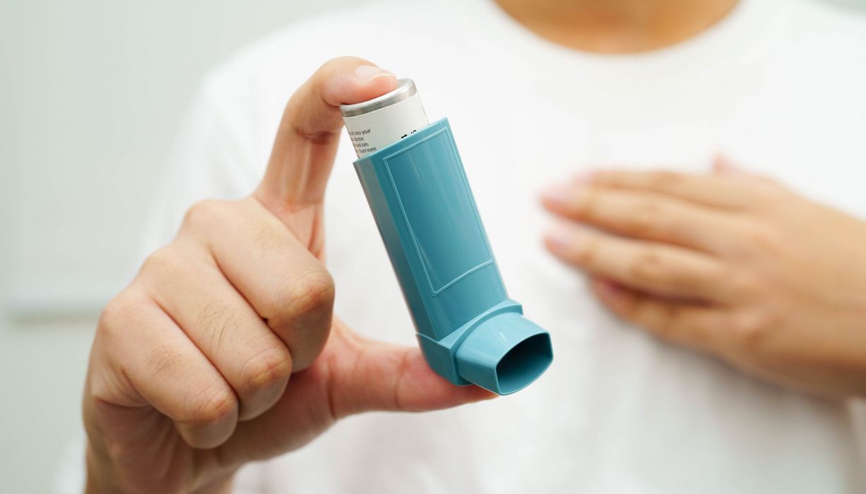 Frau, hält ein Asthmaspray in die Kamera.