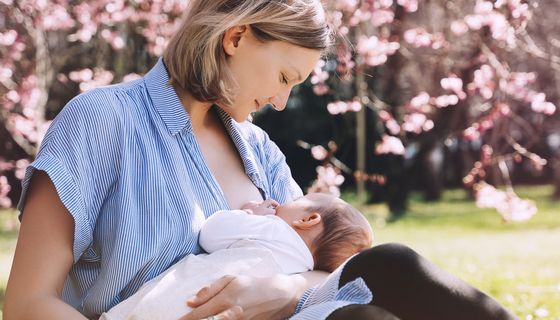 Frau stillt unter einem blühenden Kirschbaum ihr Baby.