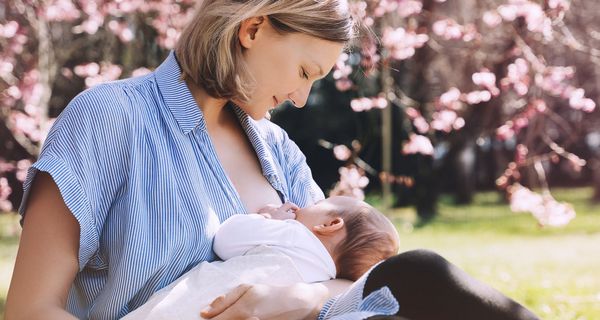 Frau stillt unter einem blühenden Kirschbaum ihr Baby.