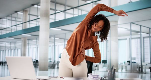Eine Frau ist vom Laptop aufgestanden und streckt sich.