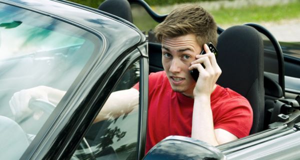 Teenager fährt Auto und telefoniert mit dem Handy.