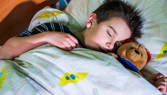 Schlafender Junge, ca. 8, mit Teddy im Arm, in buntem Bettzeug