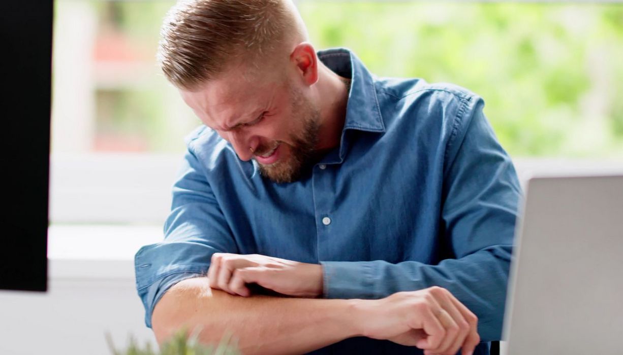 Junger Mann kratzt sich in der Ellenbogenbeuge.