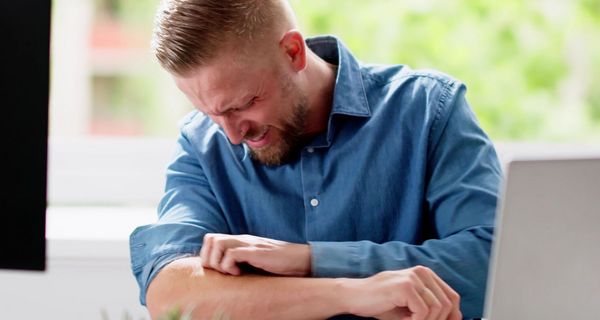 Junger Mann kratzt sich in der Ellenbogenbeuge.