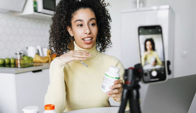 Eine Frau sitzt vor einer Handykamera in der Küche. Sie redet und hält eine weiße Dose in der Hand.