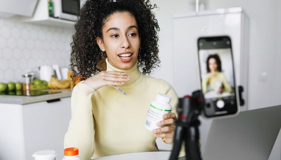 Eine Frau sitzt vor einer Handykamera in der Küche. Sie redet und hält eine weiße Dose in der Hand.