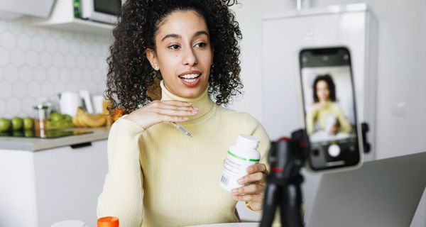 Eine Frau sitzt vor einer Handykamera in der Küche. Sie redet und hält eine weiße Dose in der Hand.