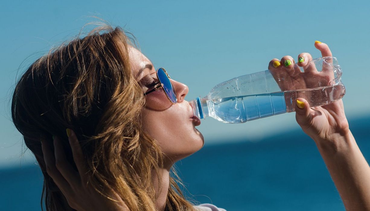 Eine Frau mit bunten Fingernägeln trinkt aus einer Plastikflasche.