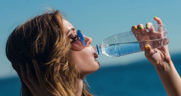 Eine Frau mit bunten Fingernägeln trinkt aus einer Plastikflasche.