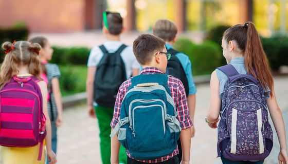 Schulkinder von hinten auf der Weg zur Schule mit unterschieldichen Schulrucksäcken.