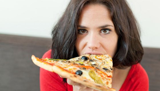 Junge dunkelhaarige Frau beißt in ein großes Stück Pizza