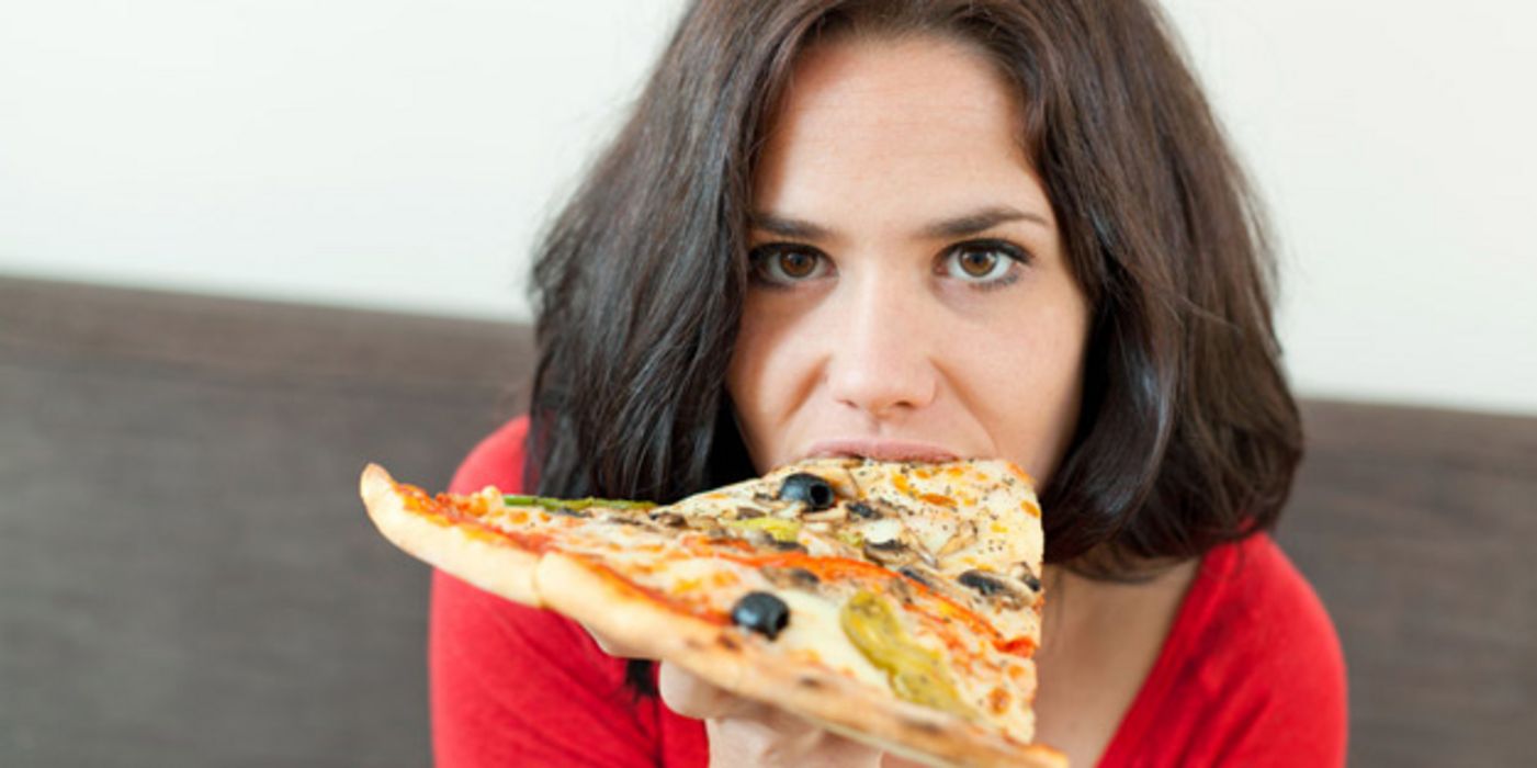 Junge dunkelhaarige Frau beißt in ein großes Stück Pizza