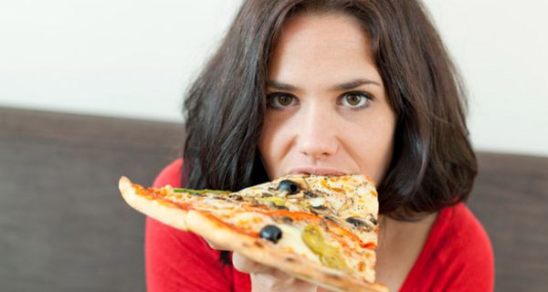 Junge dunkelhaarige Frau beißt in ein großes Stück Pizza