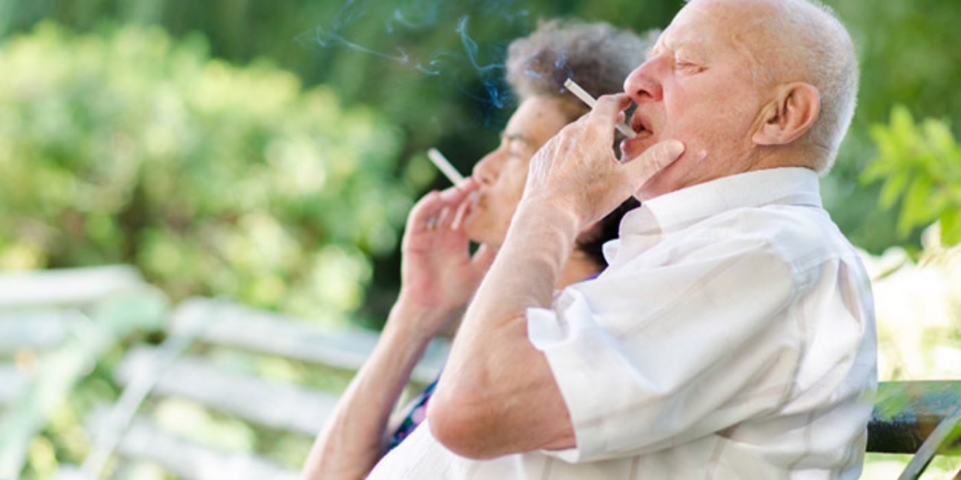 Seitenansicht Seniorenpaar auf Bank, Mann im Vordergrund, beide rauchend, Frau zum Großteil verdeckt