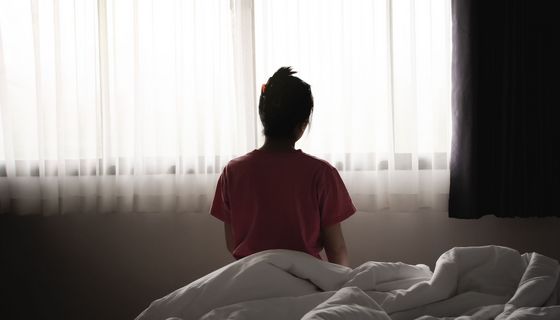 Frau, sitzt auf dem Bett, Aufnahme von hinten.