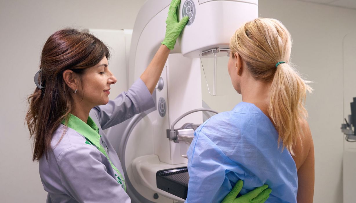 Eine Röntgentechnikerin bereitet eine Patientin für eine Mammographie vor.