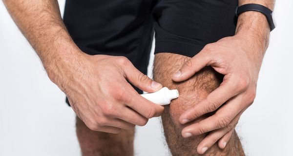 Ein Mann in Sportkleidung schmiert sich eine Salbe auf sein Knie.