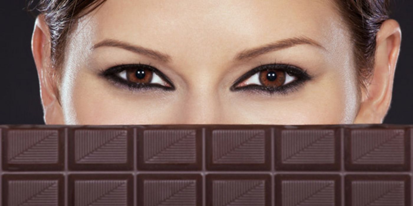 Eine junge Frau, deren Gesicht zur Hälfte von einer Tafel Schokolade verdeckt ist.