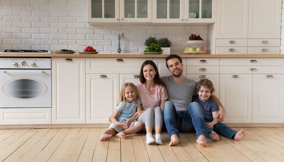 Gutgelaunte Familie mit zwei kleinen Kindern sitzt zusammen auf dem Küchenfußboden.