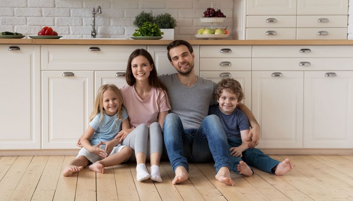 Gutgelaunte Familie mit zwei kleinen Kindern sitzt zusammen auf dem Küchenfußboden.