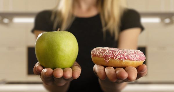 Frau, hält einen Apfel und einen Donut in der Hand.