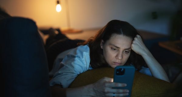 Frau, liegt im Bett und schaut auf ihr Smartphone.