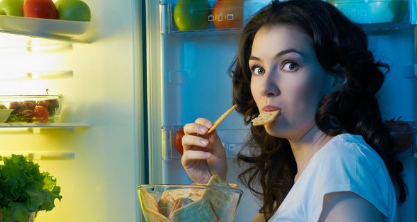 Junge Frau nachts am Kühlschrank und isst einen Snack