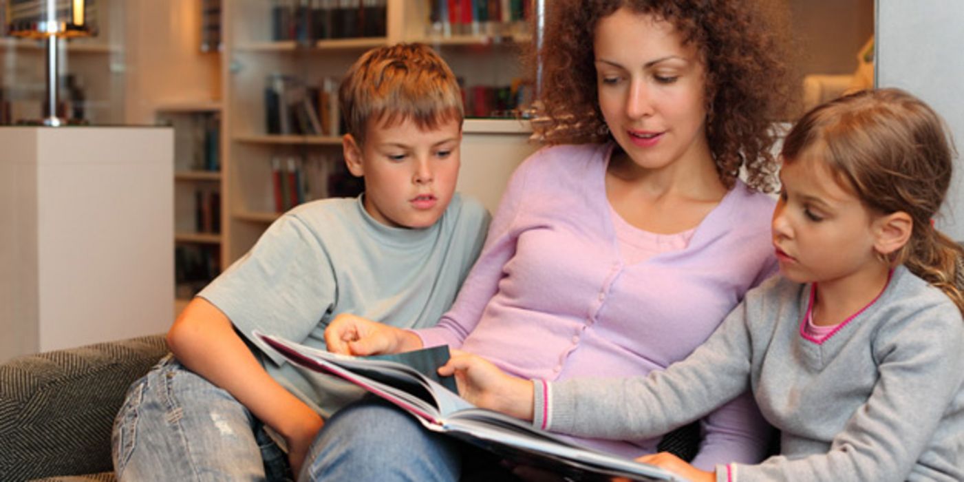 Mutter liest einem Mädchen und einem Jungen, ca. 10, 11 Jahre alt, etwas vor