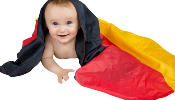 Freigestellt: Baby auf Bauch mit Deutschlandfahne über Kopf und auf Boden drapiert, lächelt in Kamera