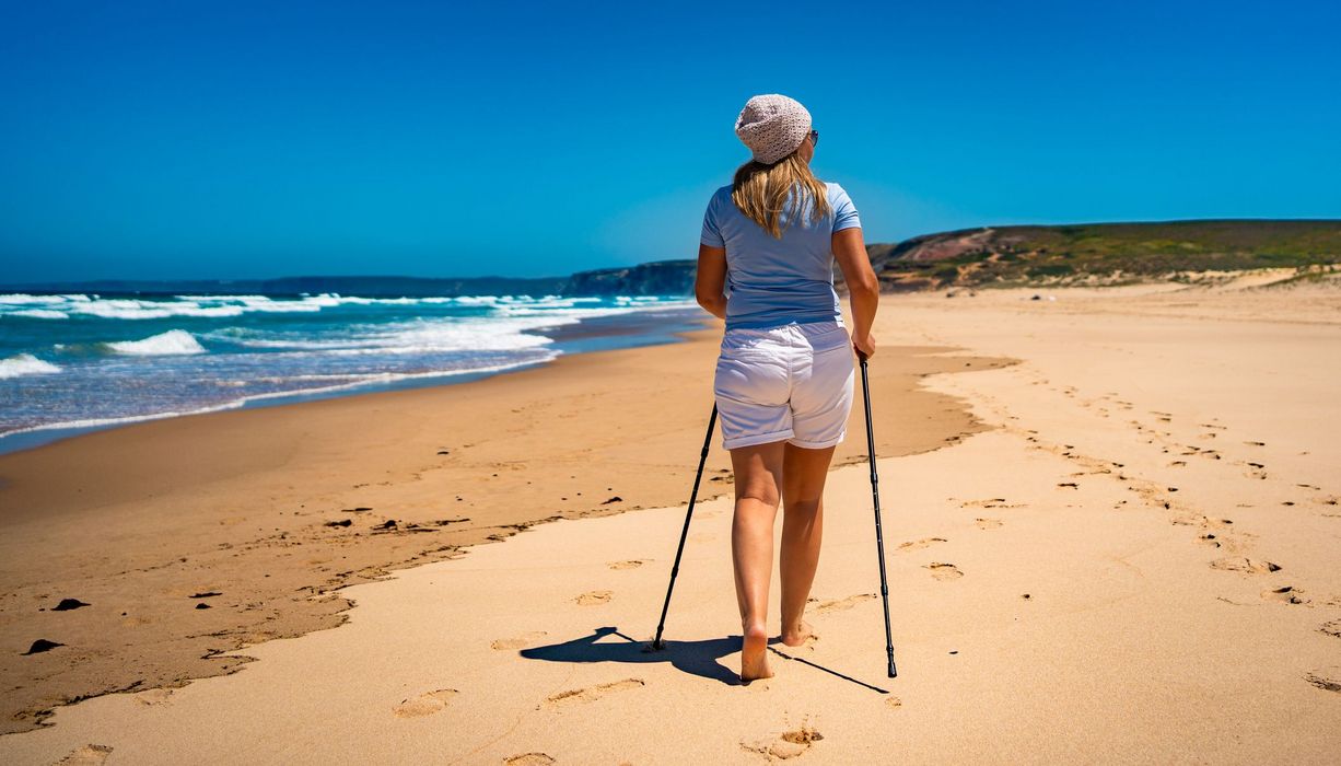 Frau geht Barfuß mit Stöcken Strand entlang