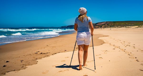 Frau geht Barfuß mit Stöcken Strand entlang