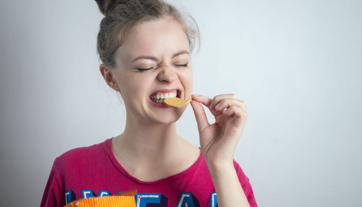 Jugendliches Mädchen, beißt in Chips.