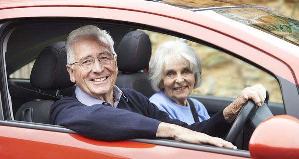 Älteres Paar sitzt in rotem Auto.