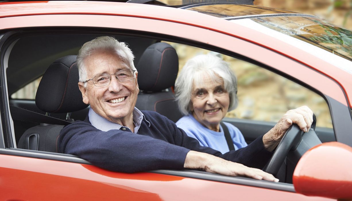 Älteres Paar sitzt in rotem Auto.