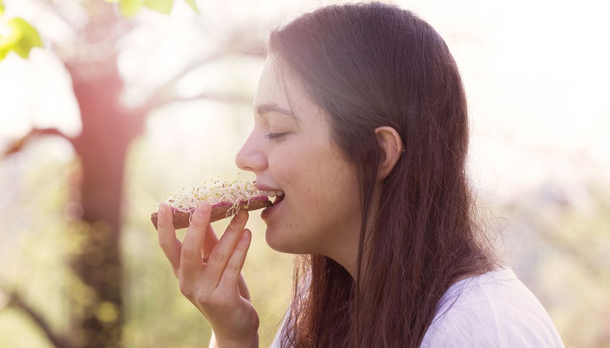 Eine Frau isst ein Brot mit Sprossen.
