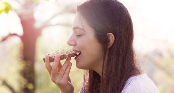 Eine Frau isst ein Brot mit Sprossen.