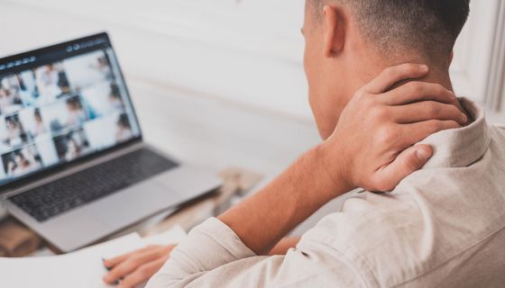Mann greift sich während einer Video-Konferenz auf dem Laptop in den Nacken.