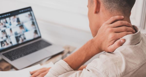 Mann greift sich während einer Video-Konferenz auf dem Laptop in den Nacken.