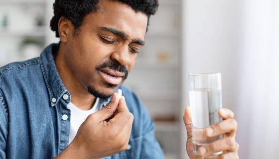 Mann nimmt eine Tablette mit einem Glas Wasser ein.